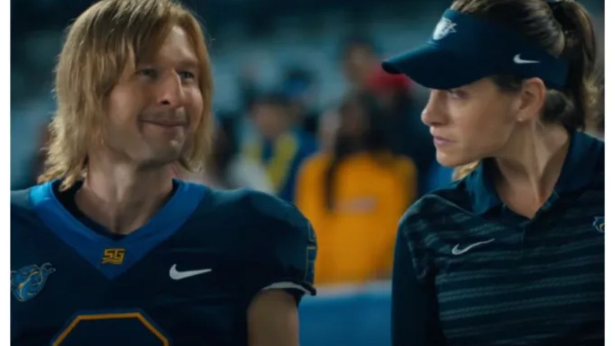 Glen Powell as Chad Powers, a college football player with long blonde hair, smiling next to a female coach in a blue visor and team polo shirt on a football field.