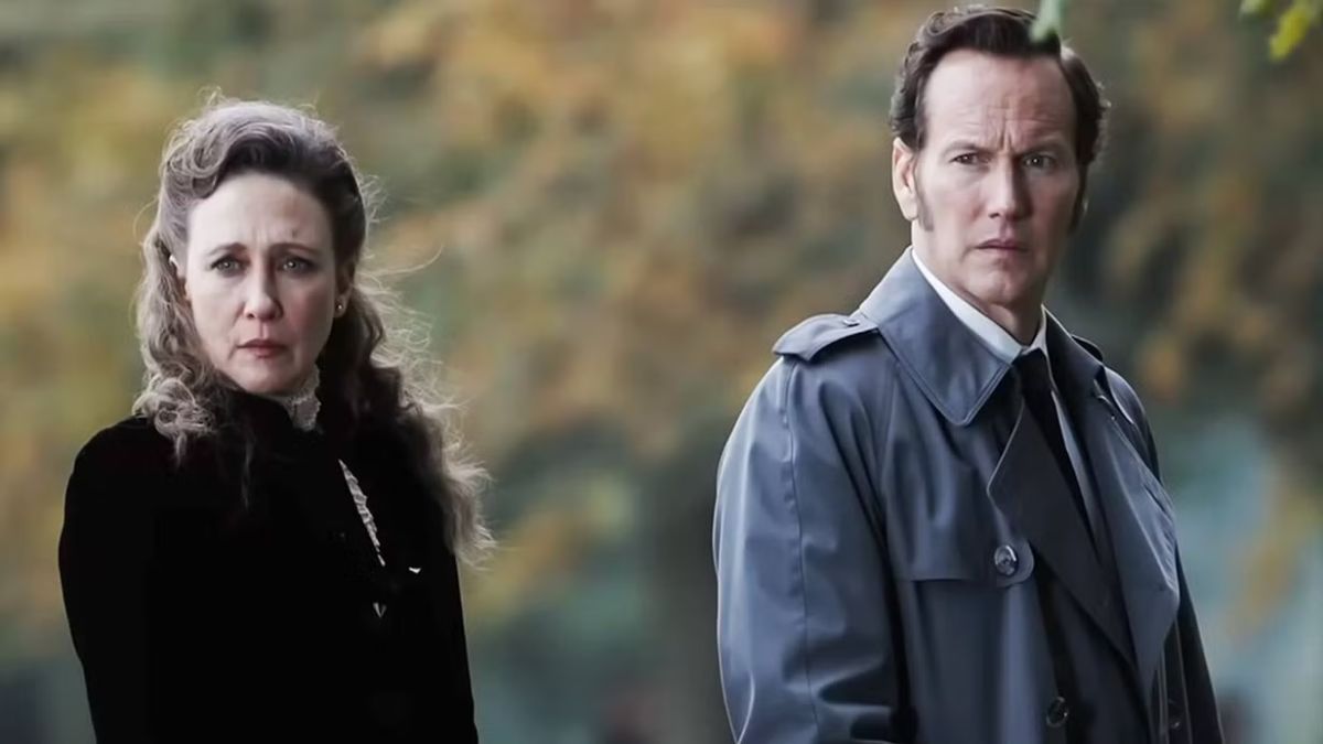 Actors Vera Farmiga and Patrick Wilson stand side by side, looking concerned. They are dressed as their characters, Ed and Lorraine Warren, in "The Conjuring: Last Rites," with a blurred, autumnal background.