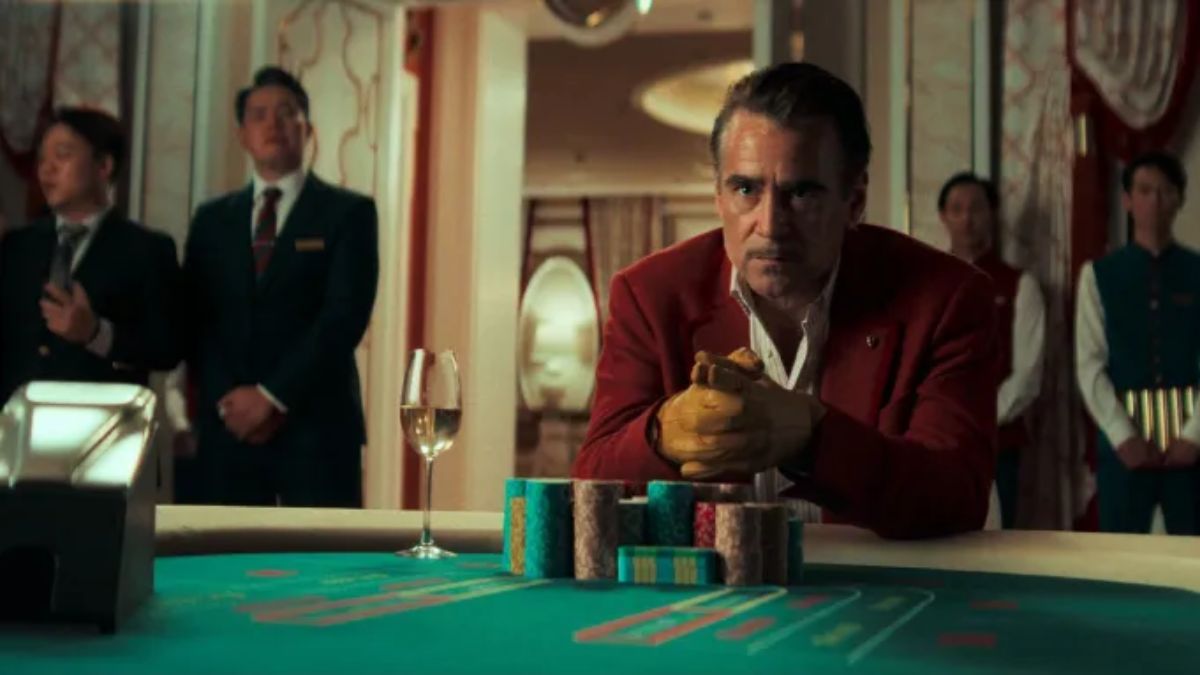 Colin Farrell as Lord Doyle, wearing a red jacket and gold gloves, sits intently at a Macau casino table with a stack of chips and a glass of champagne, flanked by casino staff.