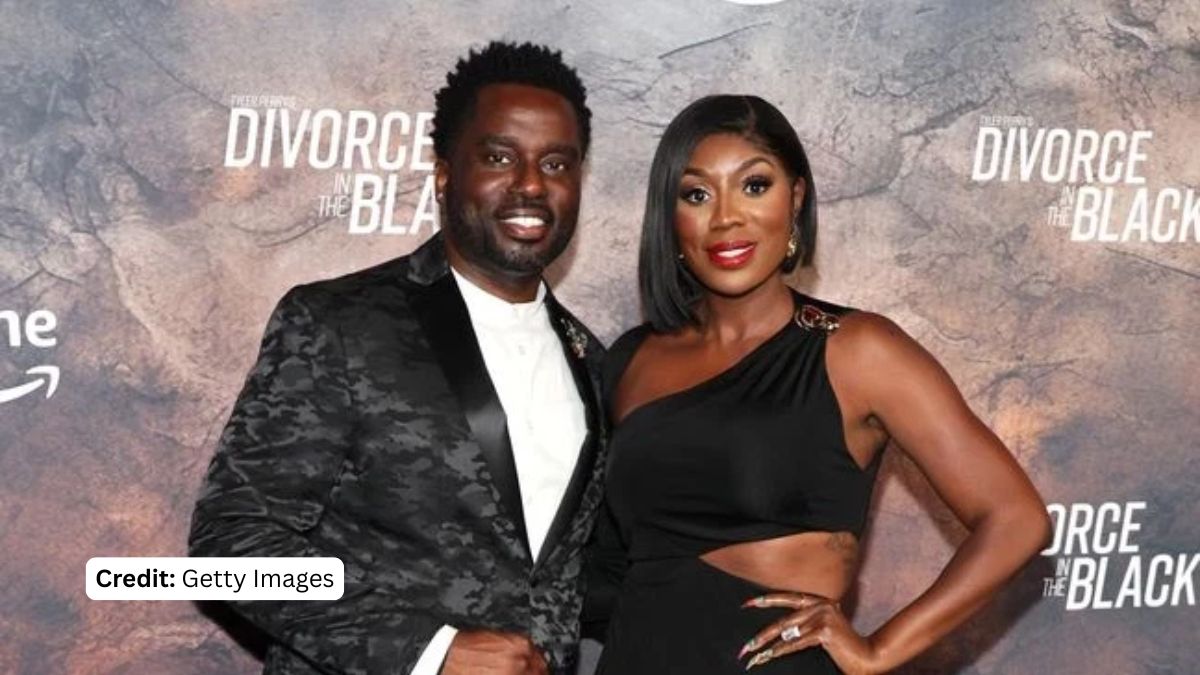 Wendy Osefo, dressed in a black one-shoulder dress with a cutout, and her husband Eddie Osefo, in a camouflage blazer, posing together on the red carpet at a movie premiere, before their fraud arrest.