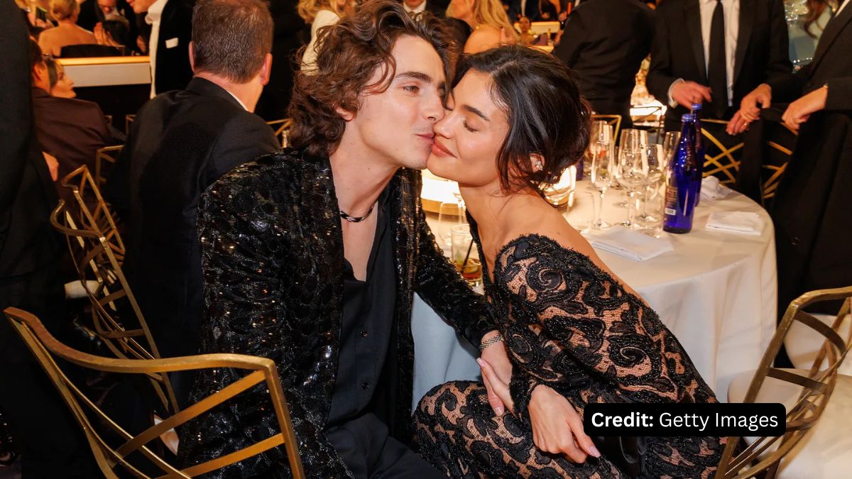 Timothée Chalamet kissing Kylie Jenner on the cheek at a formal event, with Chalamet in a black sequined jacket and Jenner in a black lace dress.