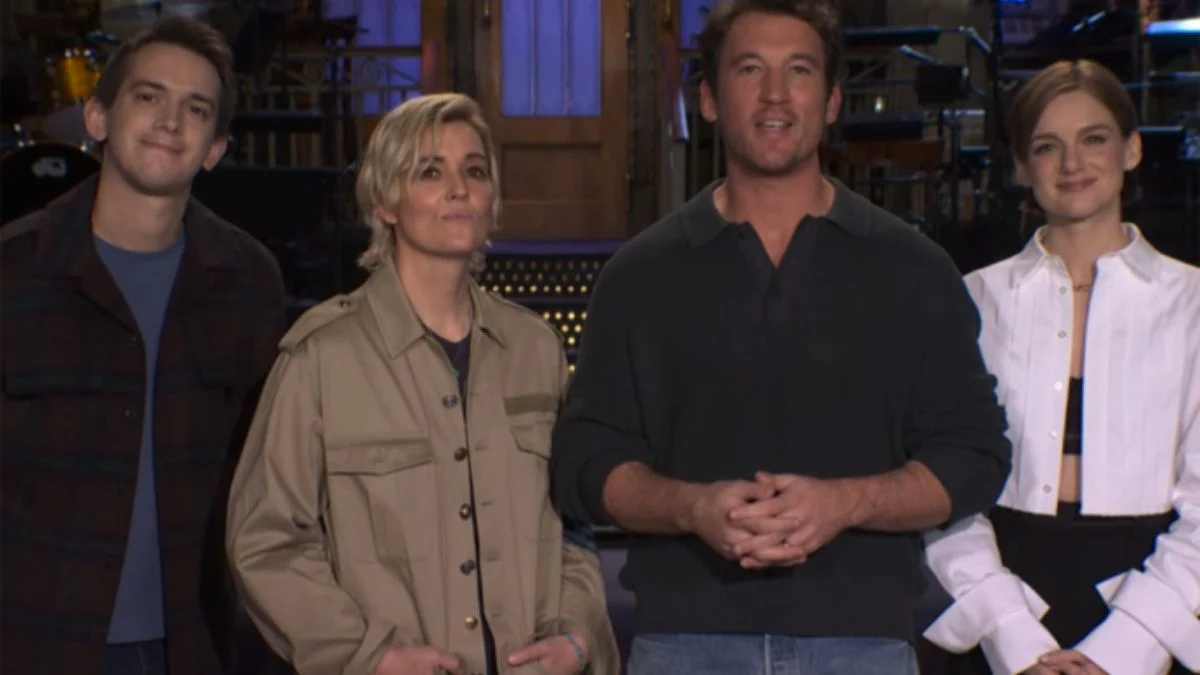 Miles Teller standing on the SNL stage with musical guest Brandi Carlile and two cast members during a promotional segment for the show.
