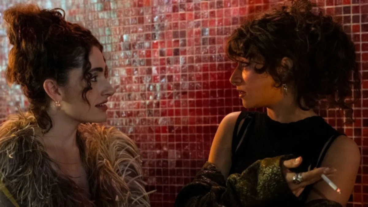 Rachel Sennott (Maia) and Odessa A'zion (Tallulah) talking intently next to a red-tiled background, possibly during a raw confrontation.