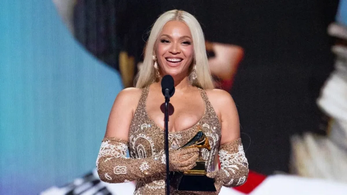 Beyoncé smiling and holding a Grammy Award on stage during a ceremony.