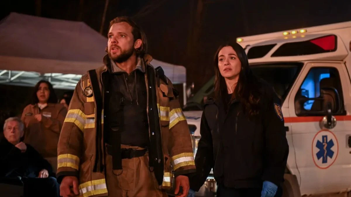 Fire Country cast members Max Thieriot as Bode Leone and Diane Farr as Sharon Leone on set in front of an ambulance.