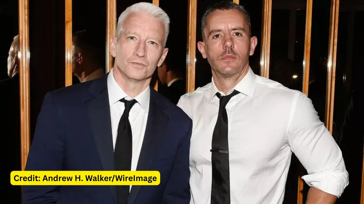 Anderson Cooper in a navy suit and Benjamin Maisani in a white shirt and black tie posing together at an indoor event.