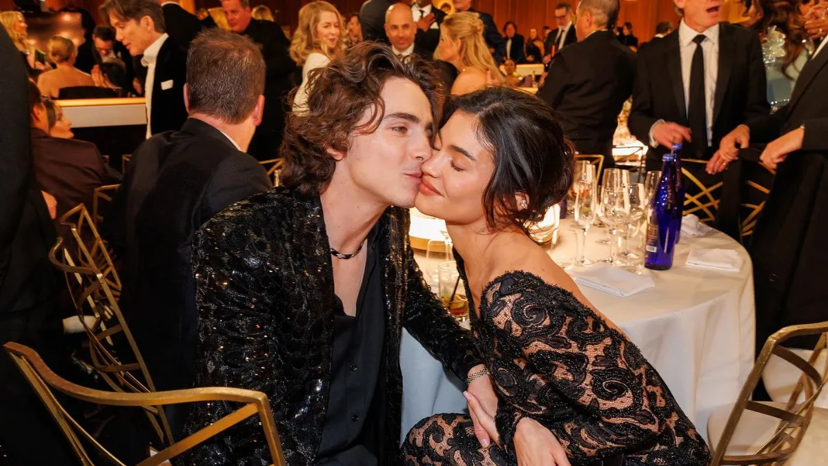 Timothée Chalamet leaning in to kiss Kylie Jenner while seated at a table during the Golden Globes.