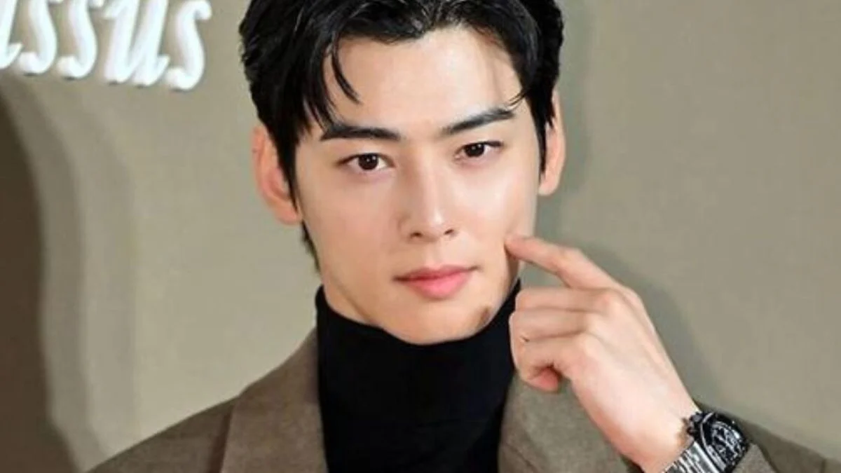 Actor Cha Eun-woo posing in a black turtleneck and brown coat at a luxury brand event.