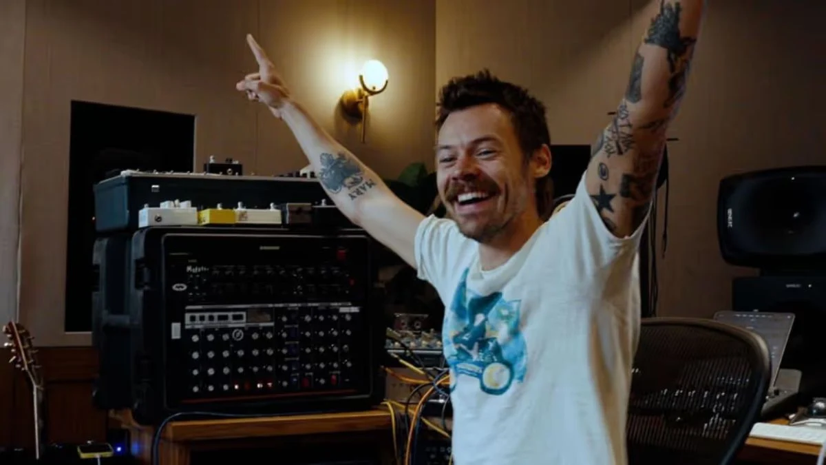 Harry Styles smiling with arms raised in a recording studio announcing his new single Aperture.