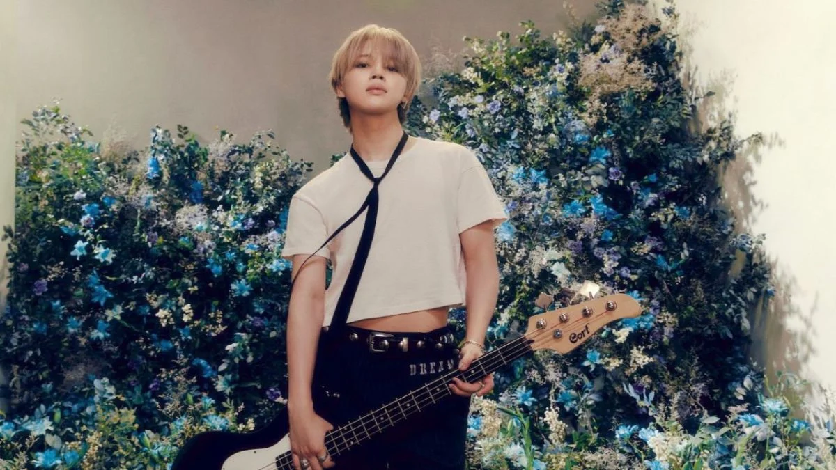 BTS member Jimin posing with a bass guitar in front of a blue floral background for his solo project.
