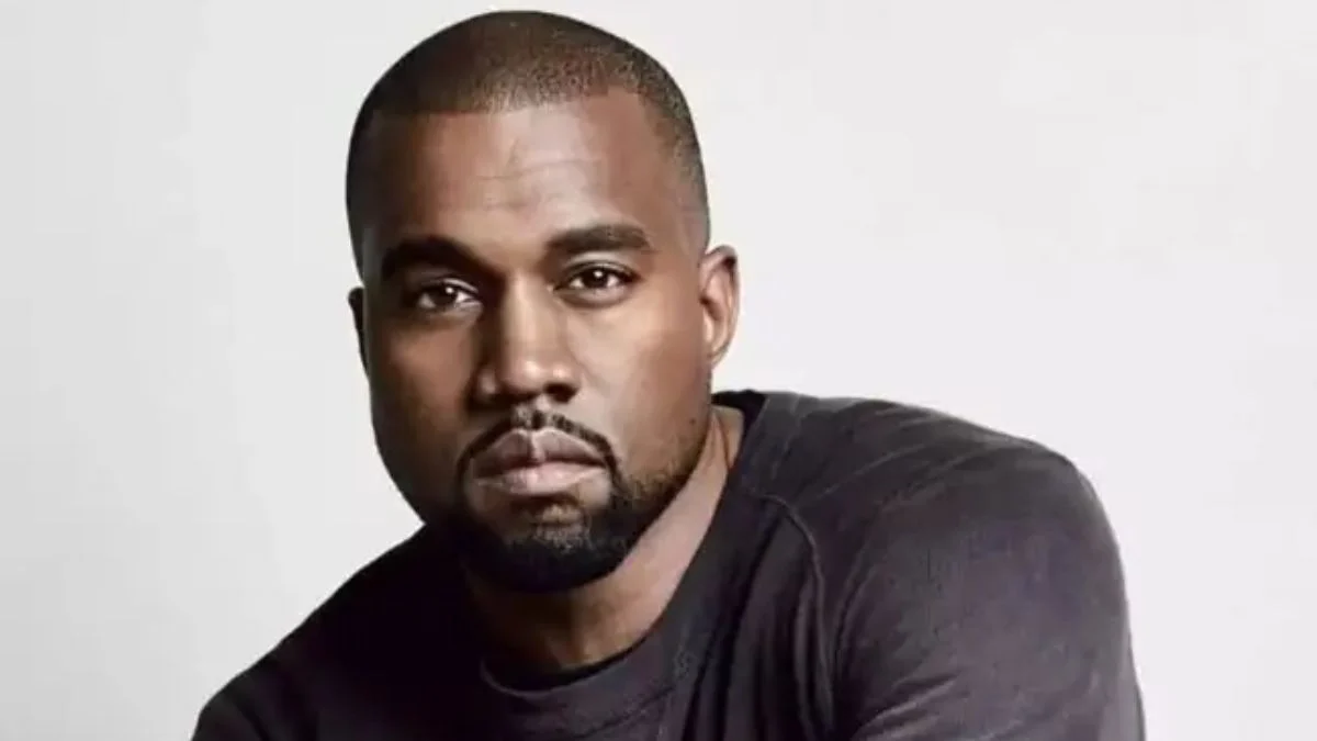 Kanye West performing live on stage with a microphone during a sold-out stadium concert.