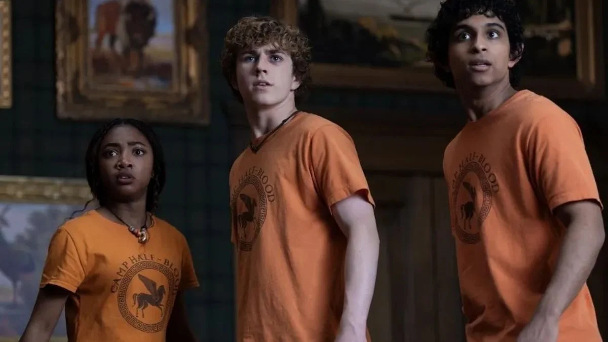 Percy, Annabeth, and Grover wearing orange Camp Half-Blood t-shirts while looking surprised inside a museum-like room.