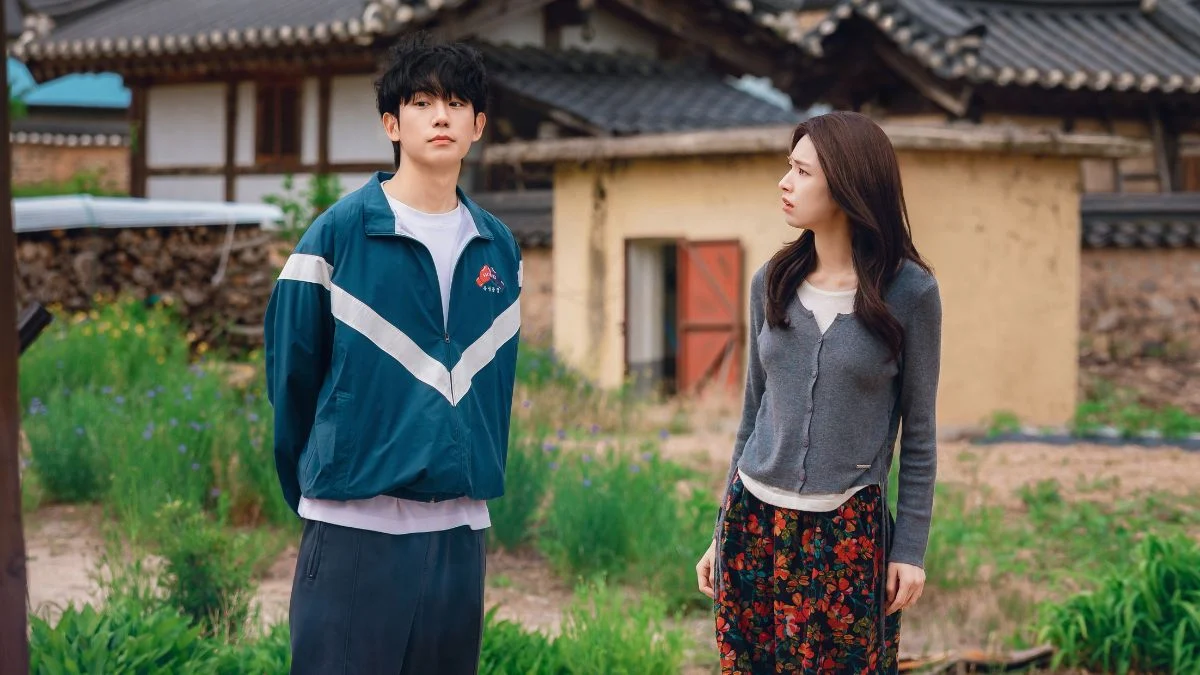Jung Hae In as Jang Tae Ha and Ha Young as Go Eun Sae standing in a traditional Korean village in Our Sticky Love.