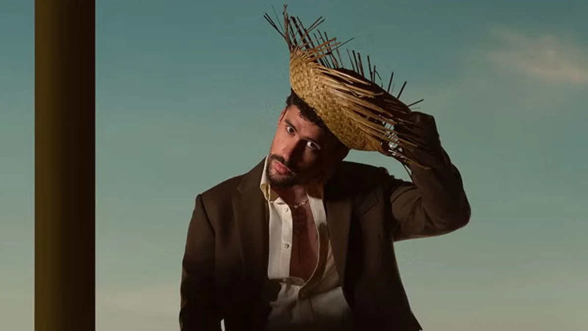 Bad Bunny wearing a traditional straw pava hat and a brown suit against a clear sky.