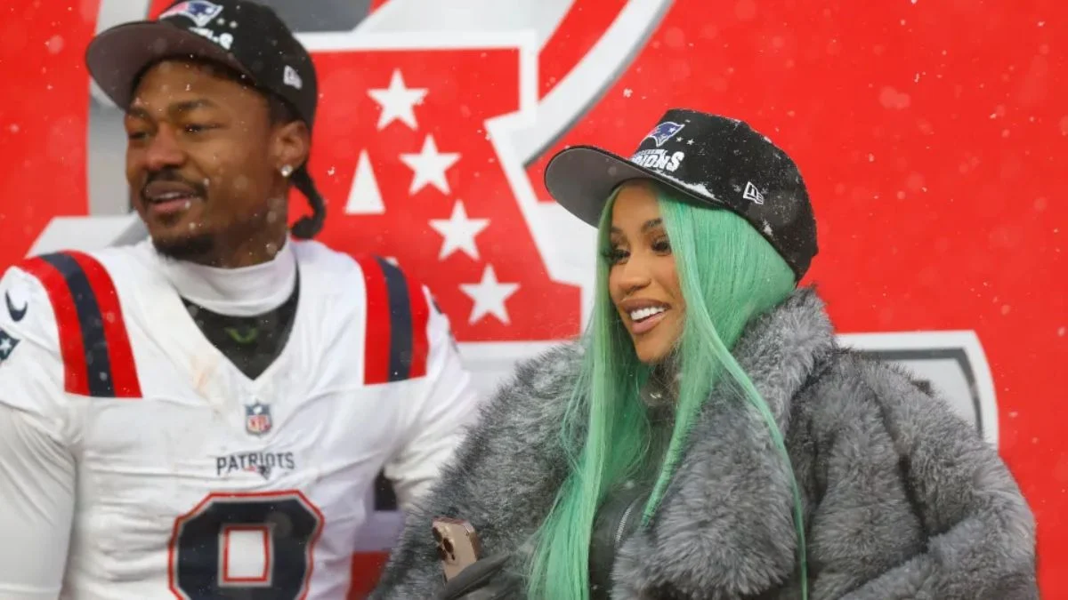 Cardi B with green hair and a fur coat standing next to Stefon Diggs in a New England Patriots jersey.