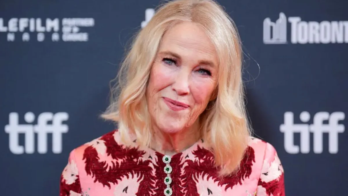 Actress Catherine O’Hara smiling on the red carpet at the Toronto International Film Festival (TIFF) wearing a pink and red patterned dress.