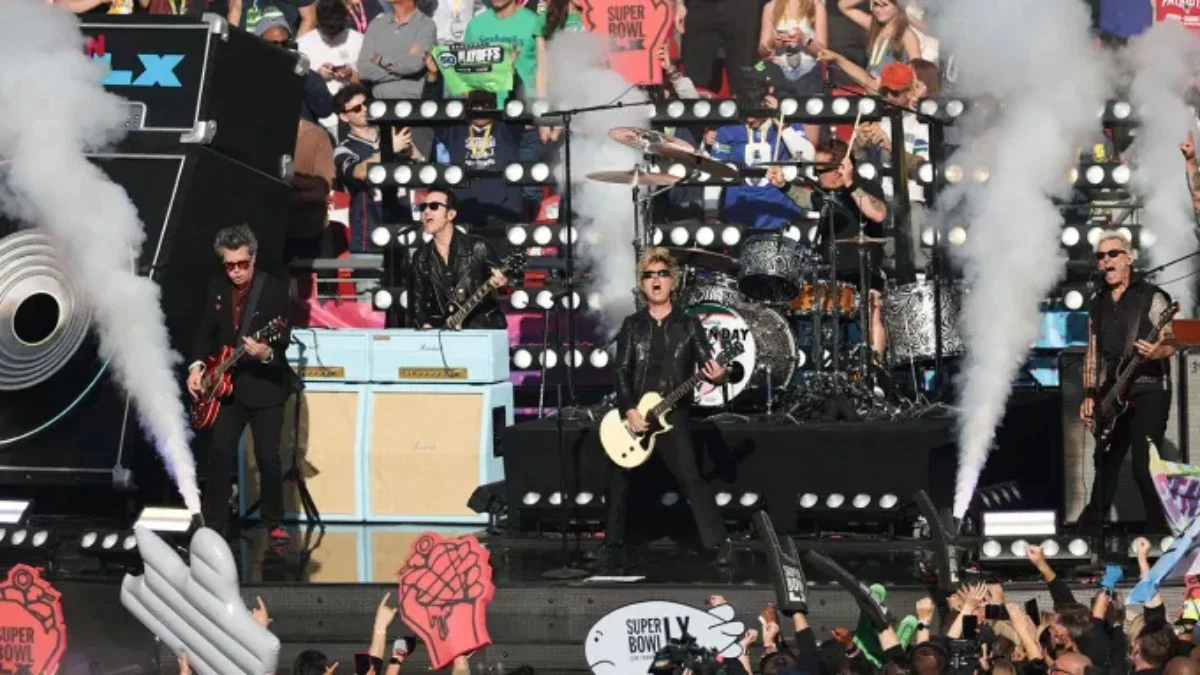 Green Day performing live at the Super Bowl LX opening ceremony with smoke effects and guitars.