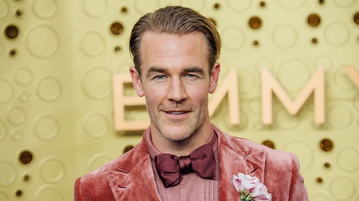A portrait of actor James Van Der Beek wearing a pink velvet suit and a maroon bowtie, smiling at the 71st Emmy Awards.