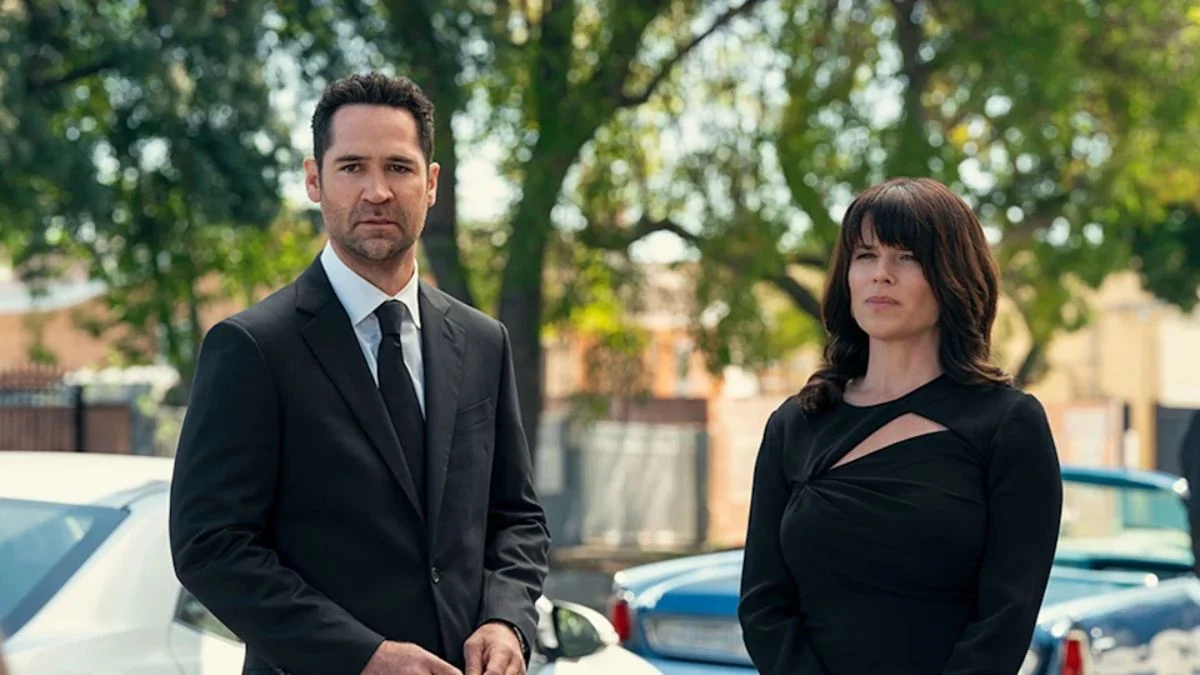 Mickey Haller (Manuel Garcia-Rulfo) and Maggie McPherson (Neve Campbell) standing together in a somber scene from The Lincoln Lawyer Season 4.