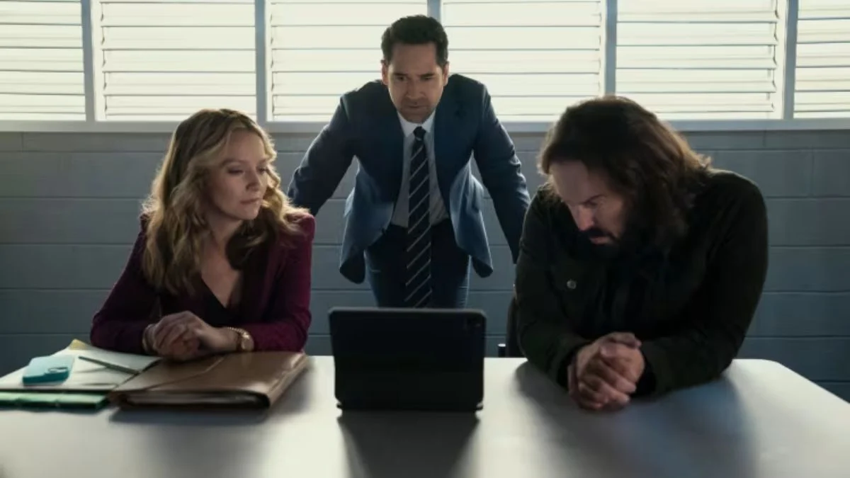 Mickey Haller leaning over a table looking at a tablet with Lorna and Cisco in an interrogation room.