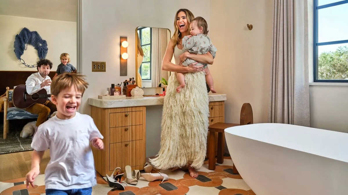 Mandy Moore laughing while holding her baby in her restored Altadena home bathroom, with her husband Taylor Goldsmith and children in the background.
