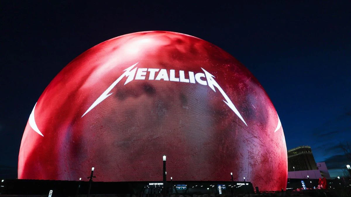 The exterior of the Sphere in Las Vegas illuminated with the white Metallica logo against a deep red glowing background at night.