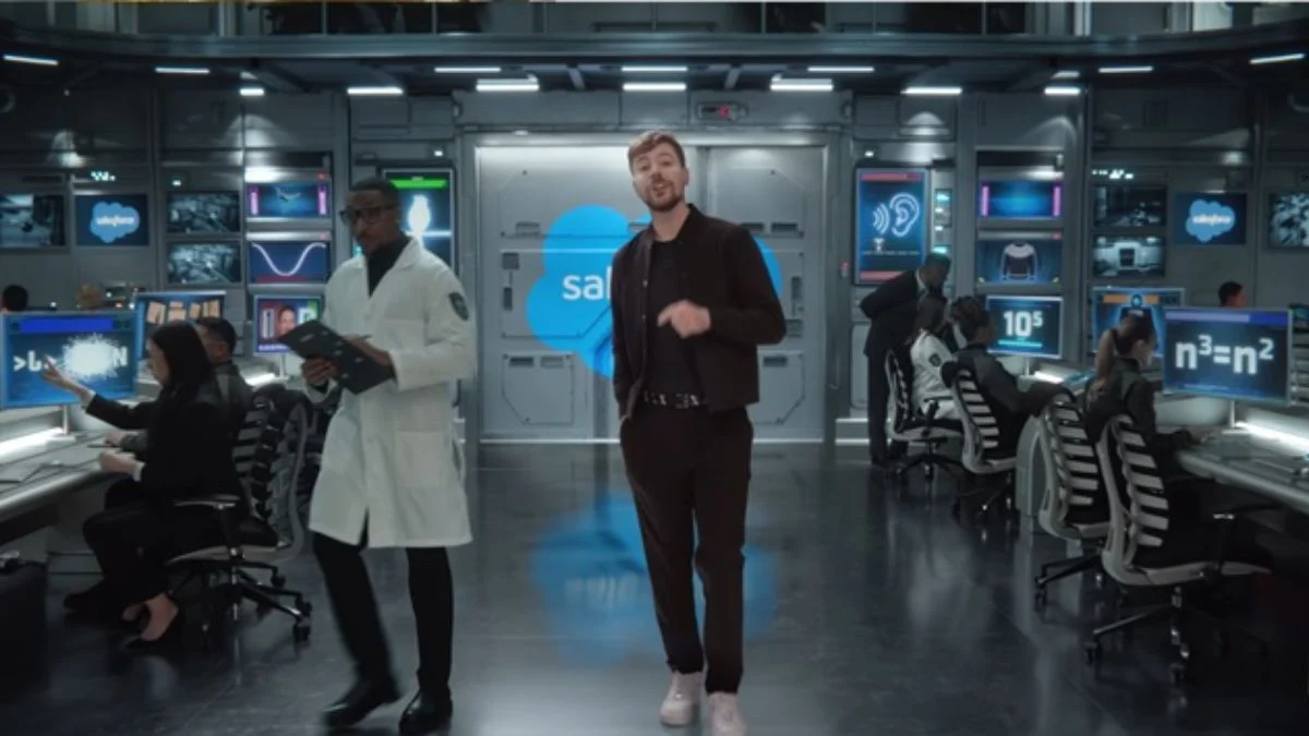 MrBeast standing in a high-tech lab with screens showing symbols like a sine wave and the Salesforce logo.