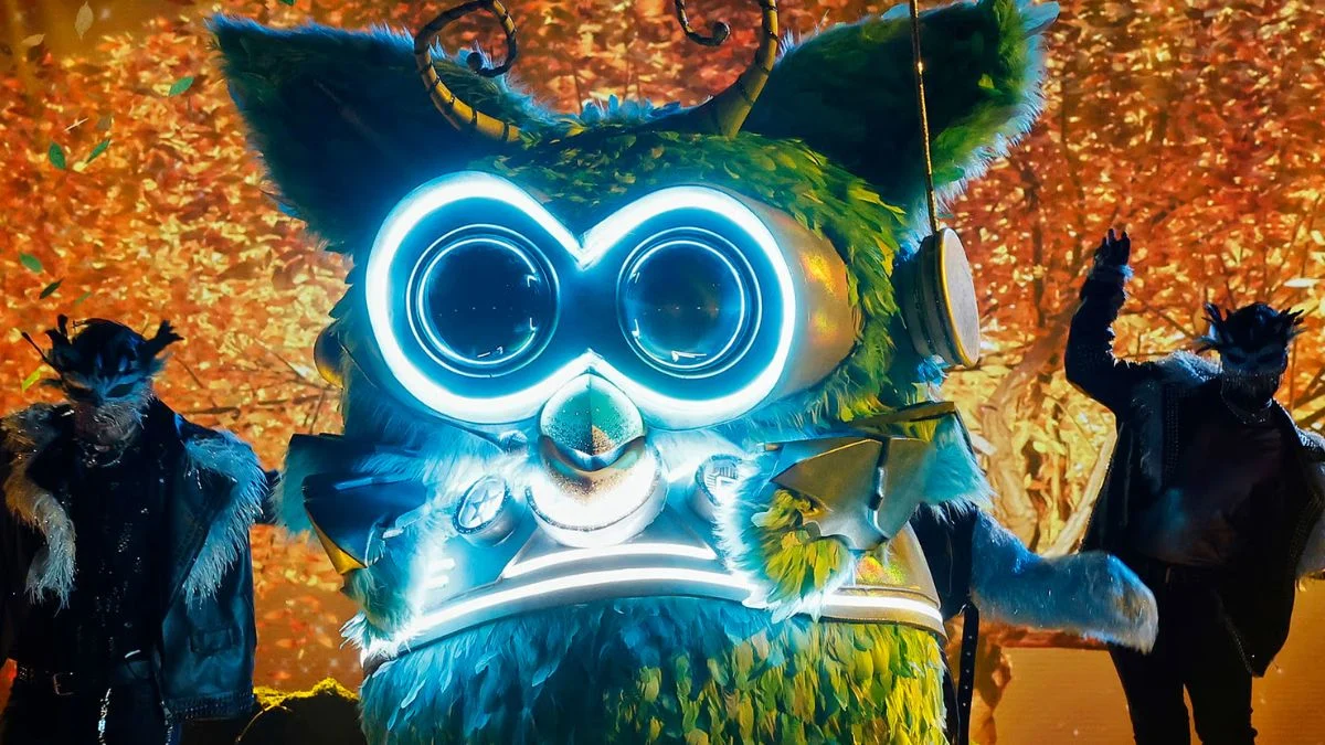 The Owl contestant on The Masked Singer Season 14 featuring a large green feathered mask with glowing blue circular eyes.