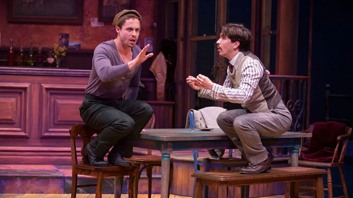 Actors Karsen Kennedy as Pablo Picasso and Cody Losinger as Albert Einstein debating on a table.