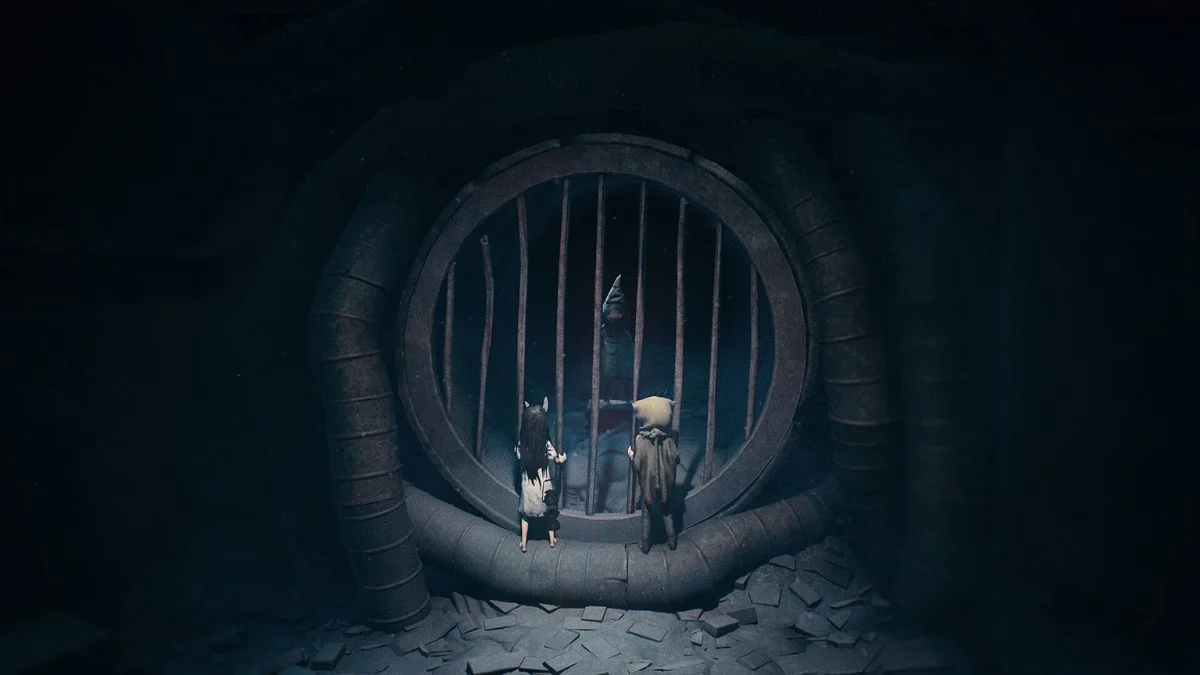 Two protagonists, a girl in a rabbit mask and a boy in a burlap hood, looking through a large circular metal grate in a dark tunnel.