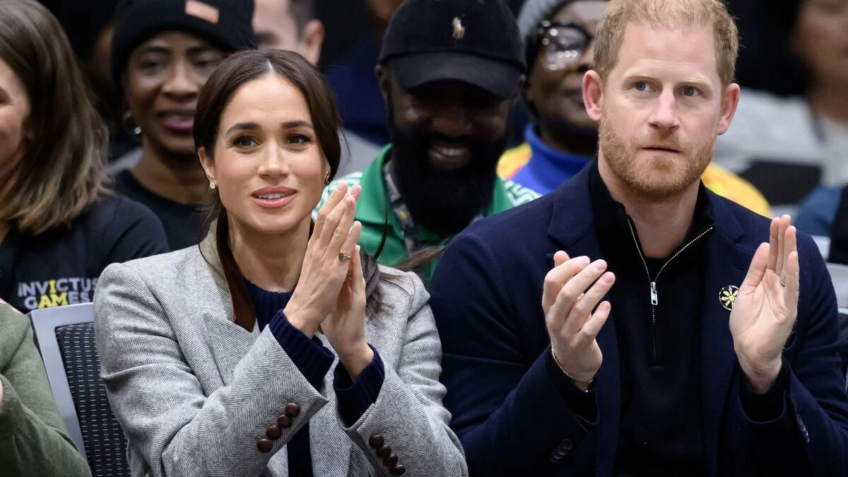 Prince Harry and Meghan Markle applauding at the Invictus Games while seated in a crowd.