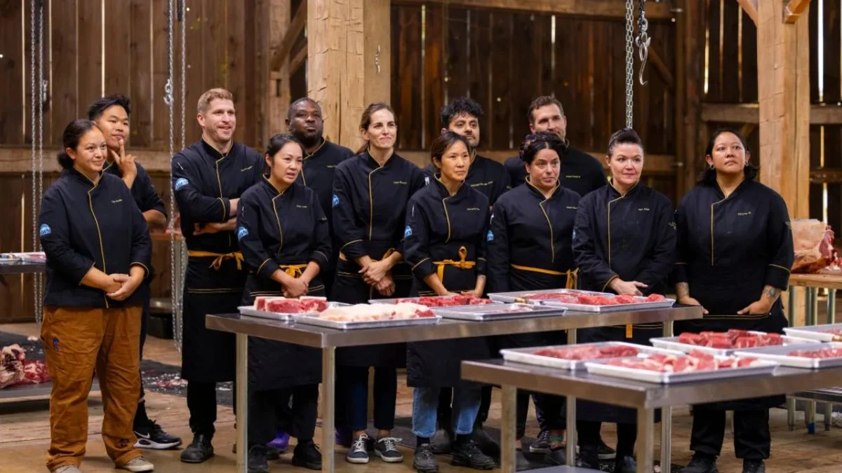 A group of elite professional chefs in black uniforms standing behind stainless steel prep tables laden with various raw beef cuts during the "Mastering the Art of Meat" challenge on America’s Culinary Cup.