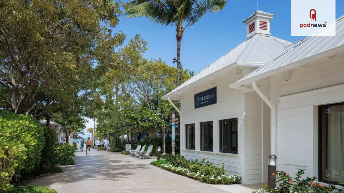 A white Caribbean-style building with a red-trimmed cupola and a sign reading 'The Studio at Baha Mar' next to a palm-lined walkway.