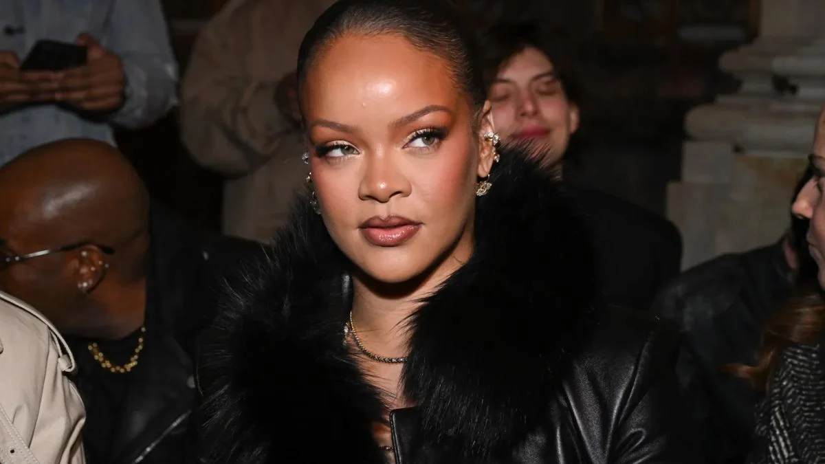 Rihanna at a high-profile event wearing a black fur-trimmed leather jacket looking off-camera.