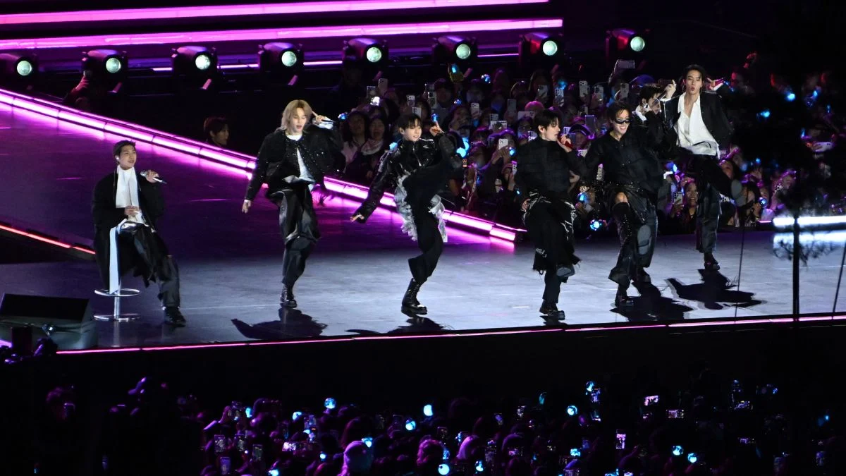 BTS performing on a large outdoor stage at night in Gwanghwamun Square, Seoul, with purple lights and a massive crowd.