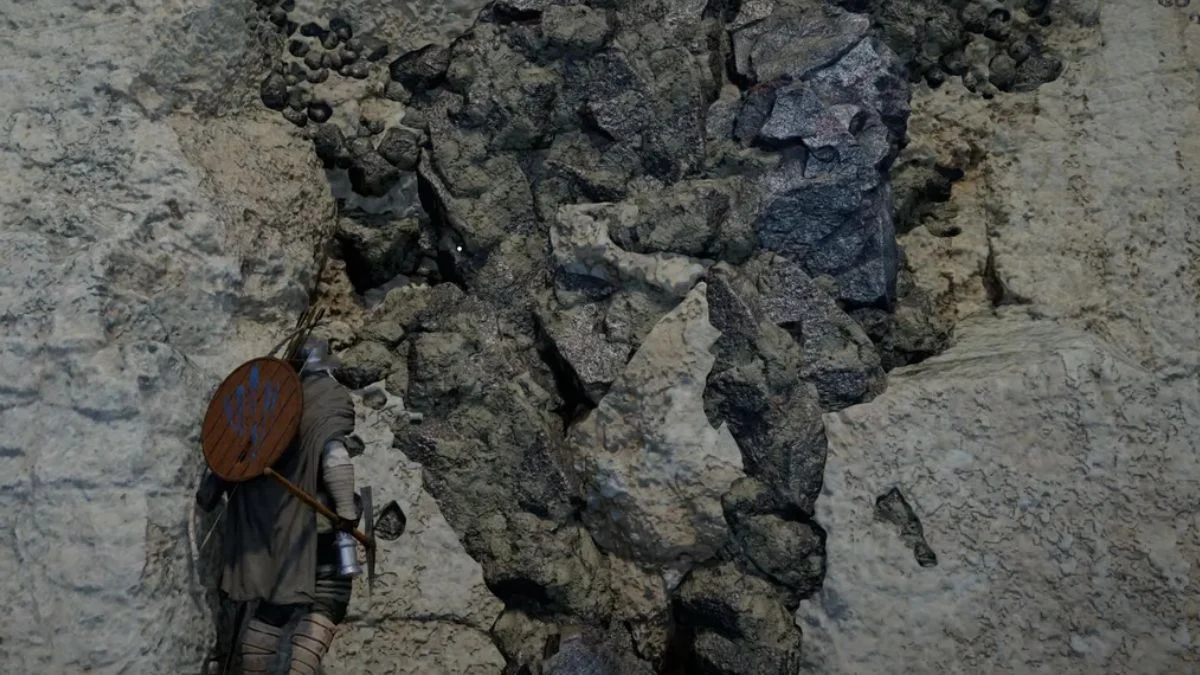 A player character standing next to a dark grey, metallic Iron Ore deposit on a light-colored stone cliff face in Crimson Desert.