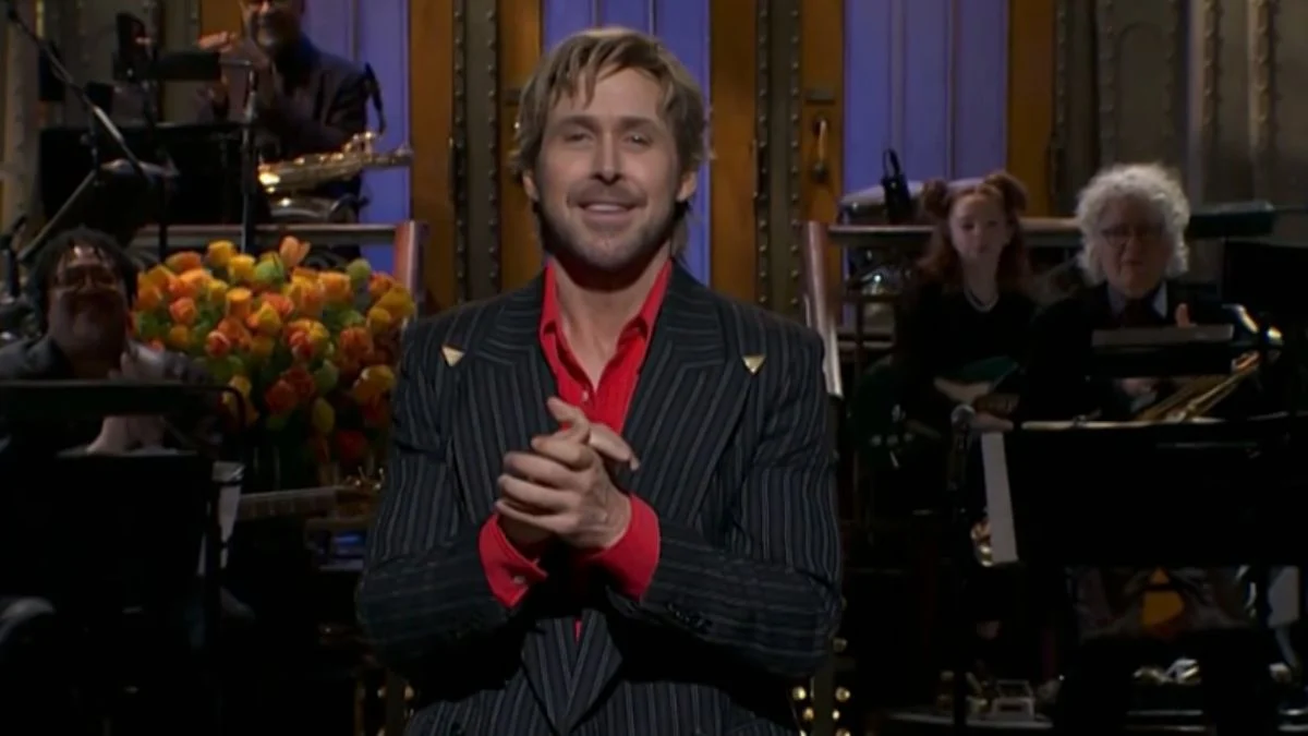 Ryan Gosling wearing a pinstripe suit and red shirt, laughing and clapping his hands during his record-breaking SNL monologue on March 7, 2026.