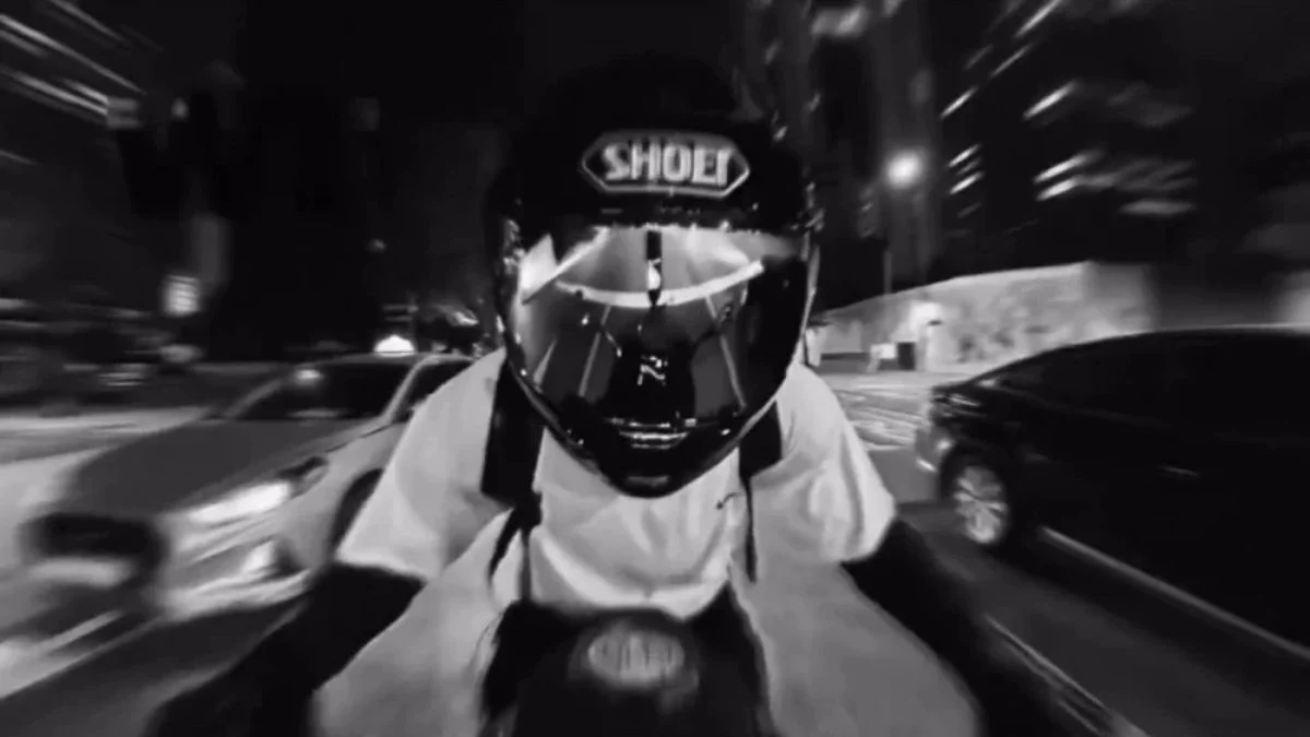 Black and white POV shot of BTS Jungkook wearing a Shoei helmet while riding a motorcycle for the Hooligan challenge.