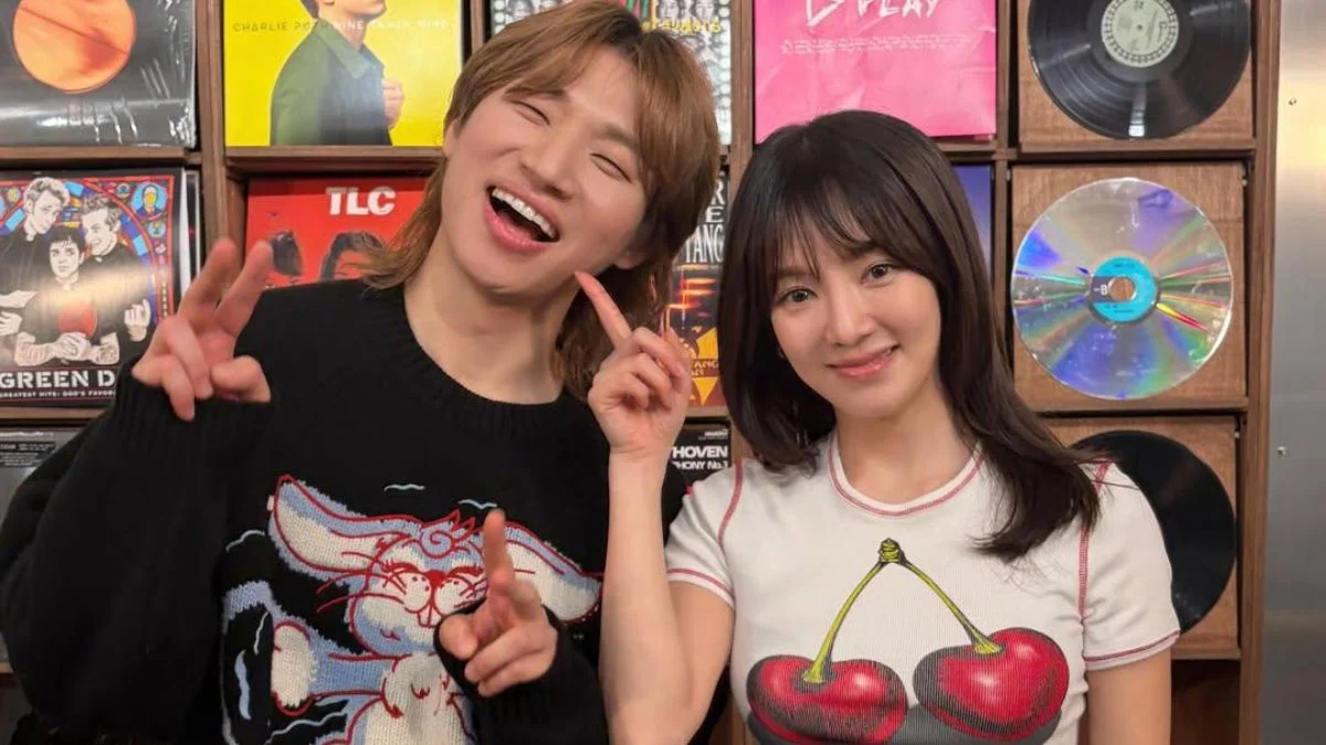 Close-up of Hyoyeon smiling and Daesung making a peace sign and laughing in front of a shelf of colorful records.