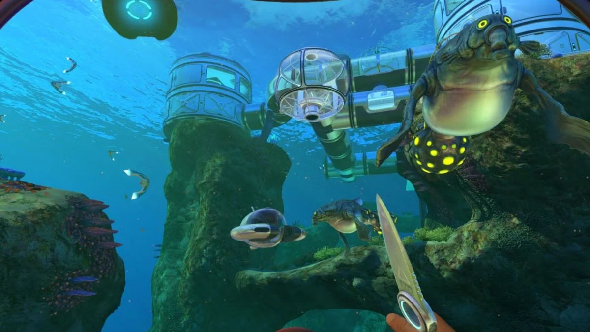 A player holding a survival knife in front of a glass underwater base habitat with Gasopods swimming in Subnautica.