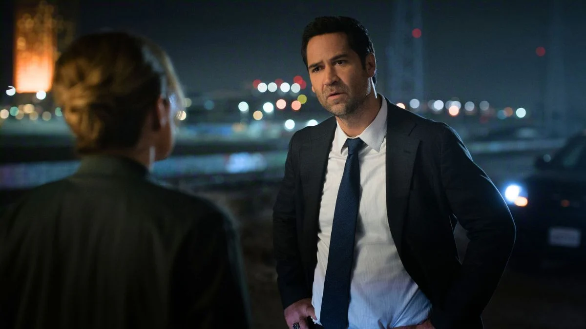 Actor Manuel Garcia-Rulfo as attorney Mickey Haller in a suit and tie, looking concerned while speaking to someone out of focus at night in a scene from Netflix's The Lincoln Lawyer.