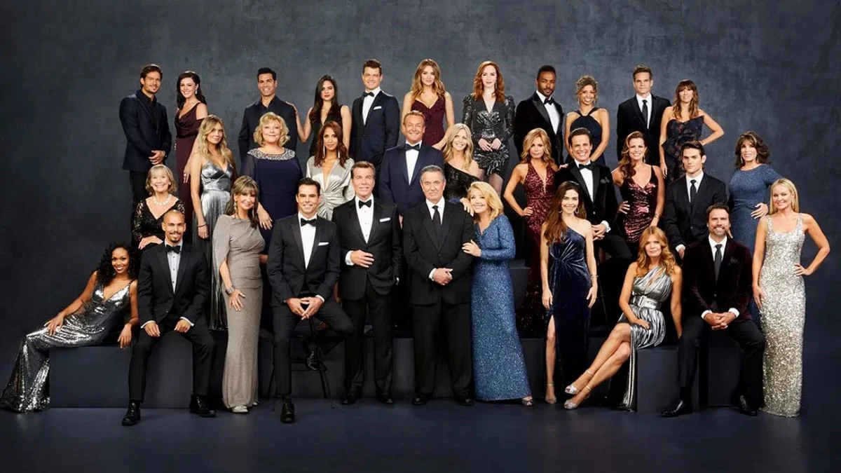 A large ensemble cast group photo of The Young and the Restless actors wearing elegant evening gowns and tuxedos against a dark grey backdrop.
