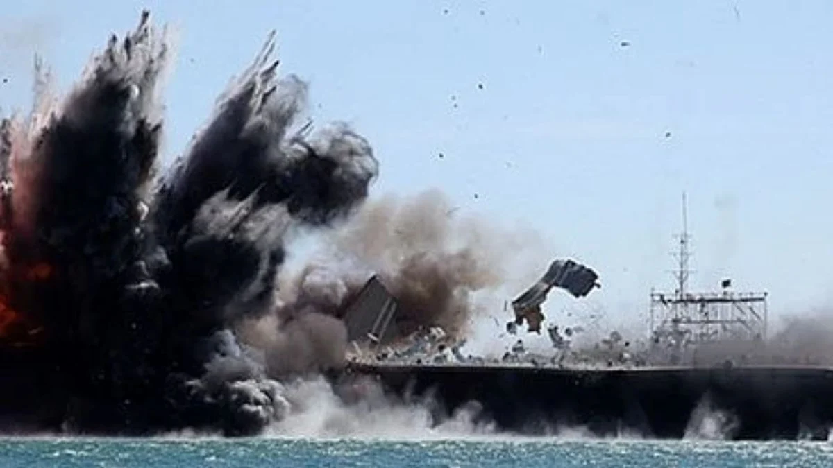 A massive explosion erupts over a naval ship at sea, launching debris, fire, and a dense plume of dark gray smoke into the air near the Strait of Hormuz.