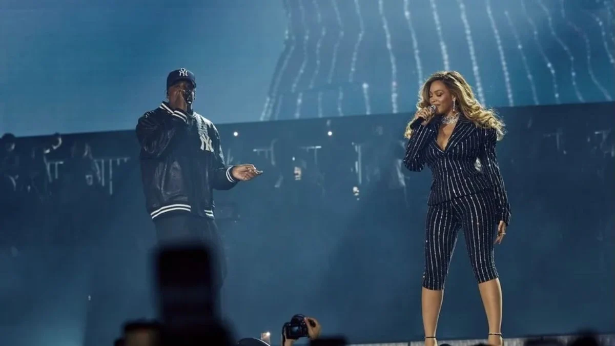 Jay-Z in a New York Yankees jacket performing alongside Beyoncé in a sparkling pinstriped suit on stage at Yankee Stadium.