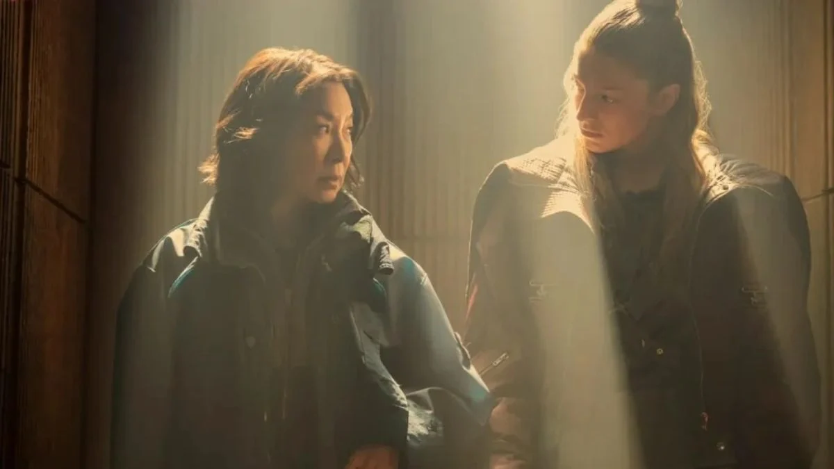 Michelle Yeoh as Olwen looking back at Hunter Schafer as Cora standing together under a beam of light in a futuristic setting.