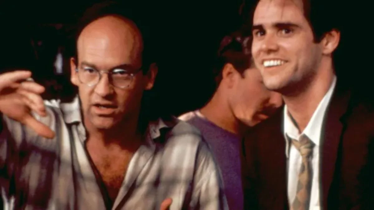 Director Chuck Russell wearing glasses and gesturing with his hands while speaking next to actor Jim Carrey on the movie set of The Mask.
