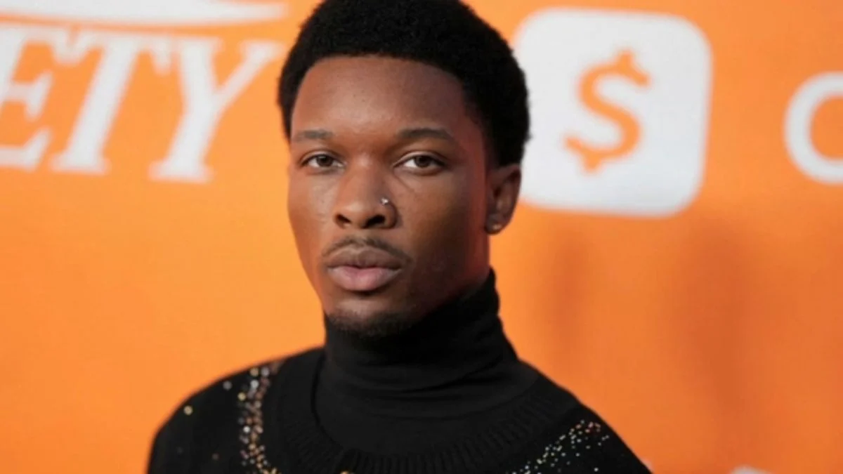 Close-up studio portrait of singer David Anthony Burke, known professionally as D4vd, wearing a black turtleneck and a nose ring while posing against a bright orange background featuring the Variety logo.