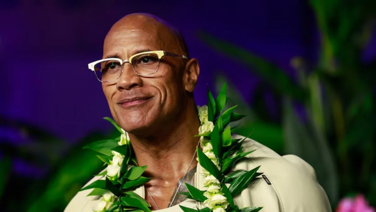Close-up of Dwayne Johnson wearing glasses and a traditional Hawaiian green leaf lei garland.