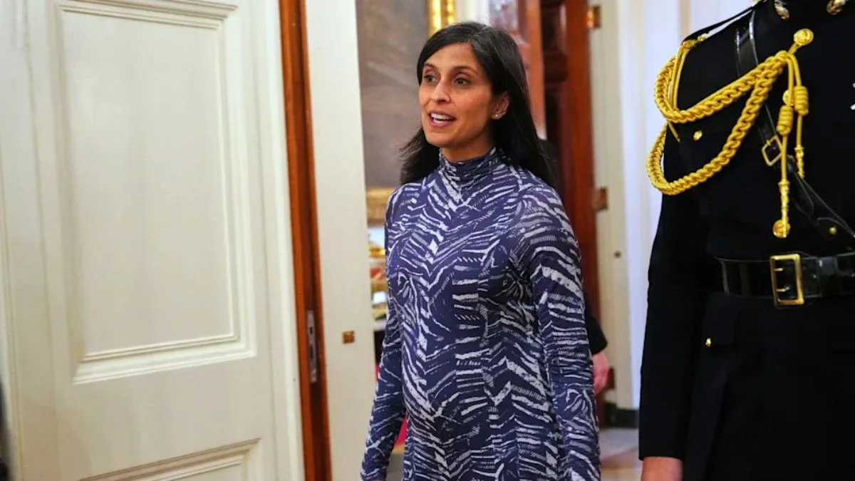 Second Lady Usha Vance wearing a patterned blue and white dress walking through a doorway next to a military official in uniform.