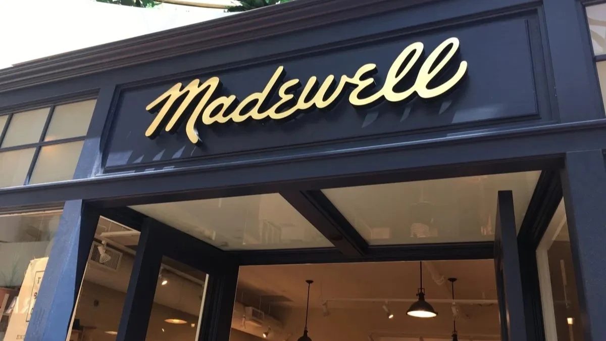 The gold script Madewell brand logo displayed on a dark, classic store facade above an open entrance.